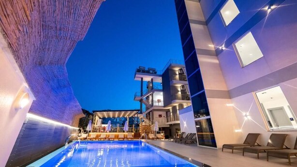 Een modern hotel met een zwembadgedeelte, ligbedden en een meerlaags gebouw met balkons.