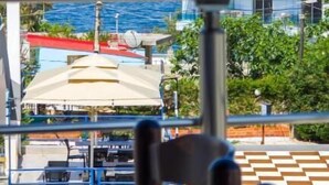 Een balkon met uitzicht op zee, een restaurant met terras en een gebouw met een rood dak.