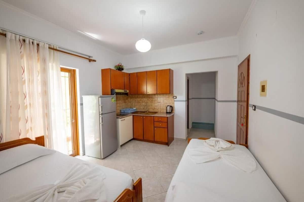 Habitación de hotel compacta con dos camas individuales, kitchenette y baño pequeño.