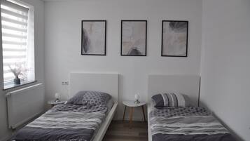Ein Schlafzimmer mit zwei Betten, einem kleinen Tisch und drei abstrakten Bildern an der Wand.