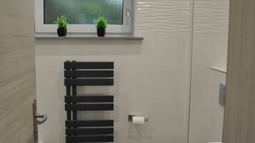 Ein modernes Badezimmer mit Toilette, einem schwarzen Handtuchhalter, einem schwarzen Teppich und einem Fenster mit zwei Blumentöpfen.