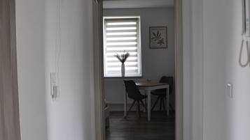 Ein Flur, der zu einem Essbereich mit Tisch und Stühlen führt, mit einem Fenster mit Jalousien und einer Pflanze an der Wand.