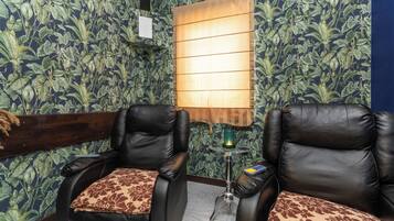 A room with two leather chairs, a small table with a lamp, and a wall with a leafy pattern.