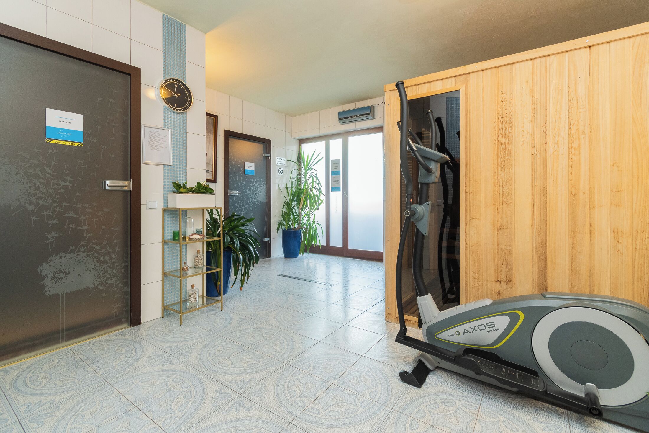 Un vestíbulo de hotel con mostrador de recepción, un reloj, una planta y una cinta de correr.