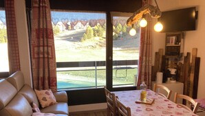 Una habitación acogedora con un sofá de cuero, una mesa de comedor con mantel estampado en forma de corazón y vistas a un paisaje verde a través de amplios ventanales.