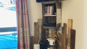 Una habitación con un televisor montado en la pared, una estantería con DVDs, una cafetera y un refrigerador pequeño.