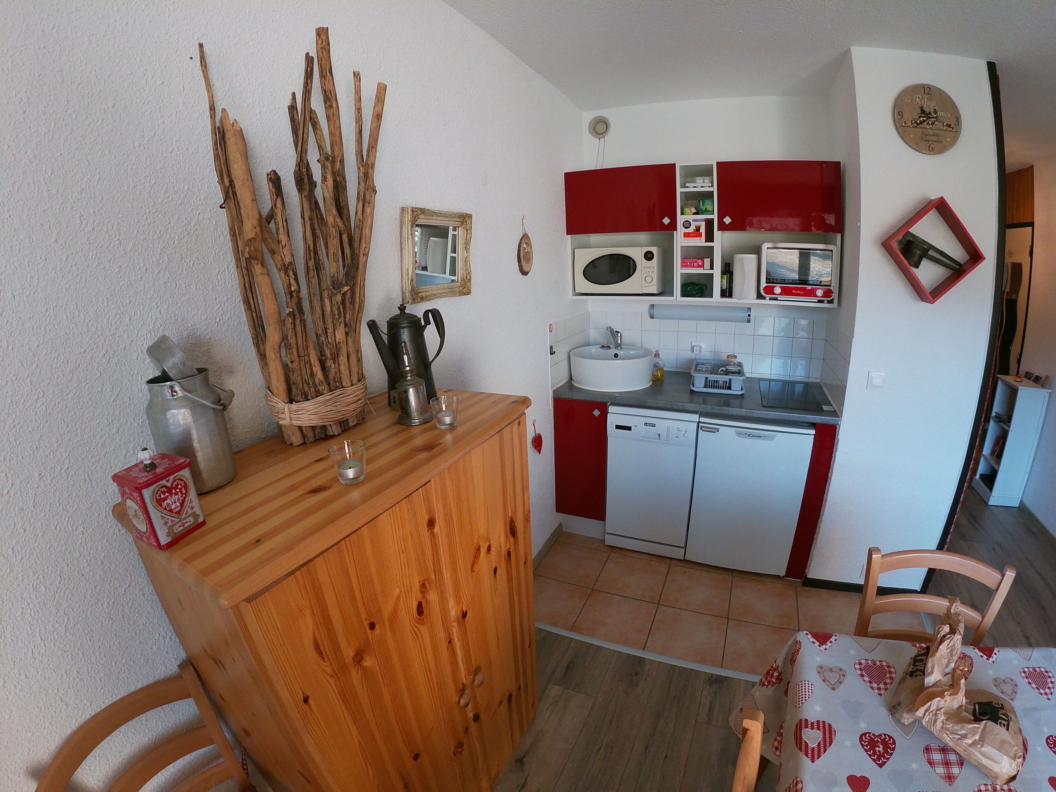 A compact kitchen with a wooden cabinet, a microwave, a sink, and red cabinets.