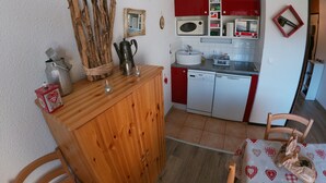 Una cocina compacta con un armario de madera, un microondas, un lavamanos y gabinetes rojos.