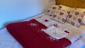 Una cama con colcha roja y blanca, almohadas estampadas con motivos de corazones y cabecera de madera.