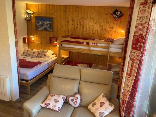 A cozy room with bunk beds, a sofa with heart-patterned cushions, wooden walls, and a painting of mountains. - Studio Yomeo - LA JOUE DU LOUP - Pied des pistes - 30 M² - 5 Pers 3 +++ (Dévoluy)