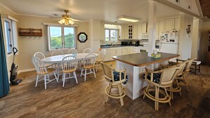 A spacious kitchen with white cabinets, a central island, and a dining area with white chairs. - 5-bedroom house in tranquil Corolla North Carolina OBX 4x4 Carova (Corolla)