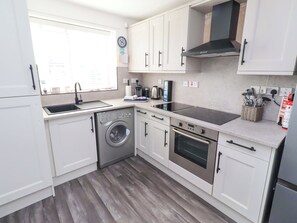 A compact kitchen with a washing machine, oven, and a large window. - Sea Shore (Seahouses)