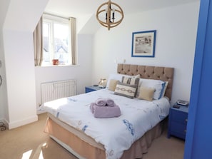 A bedroom with a bed, a window, a radiator, a nightstand, a lamp, and a framed picture on the wall. - Sea Shore (Seahouses)