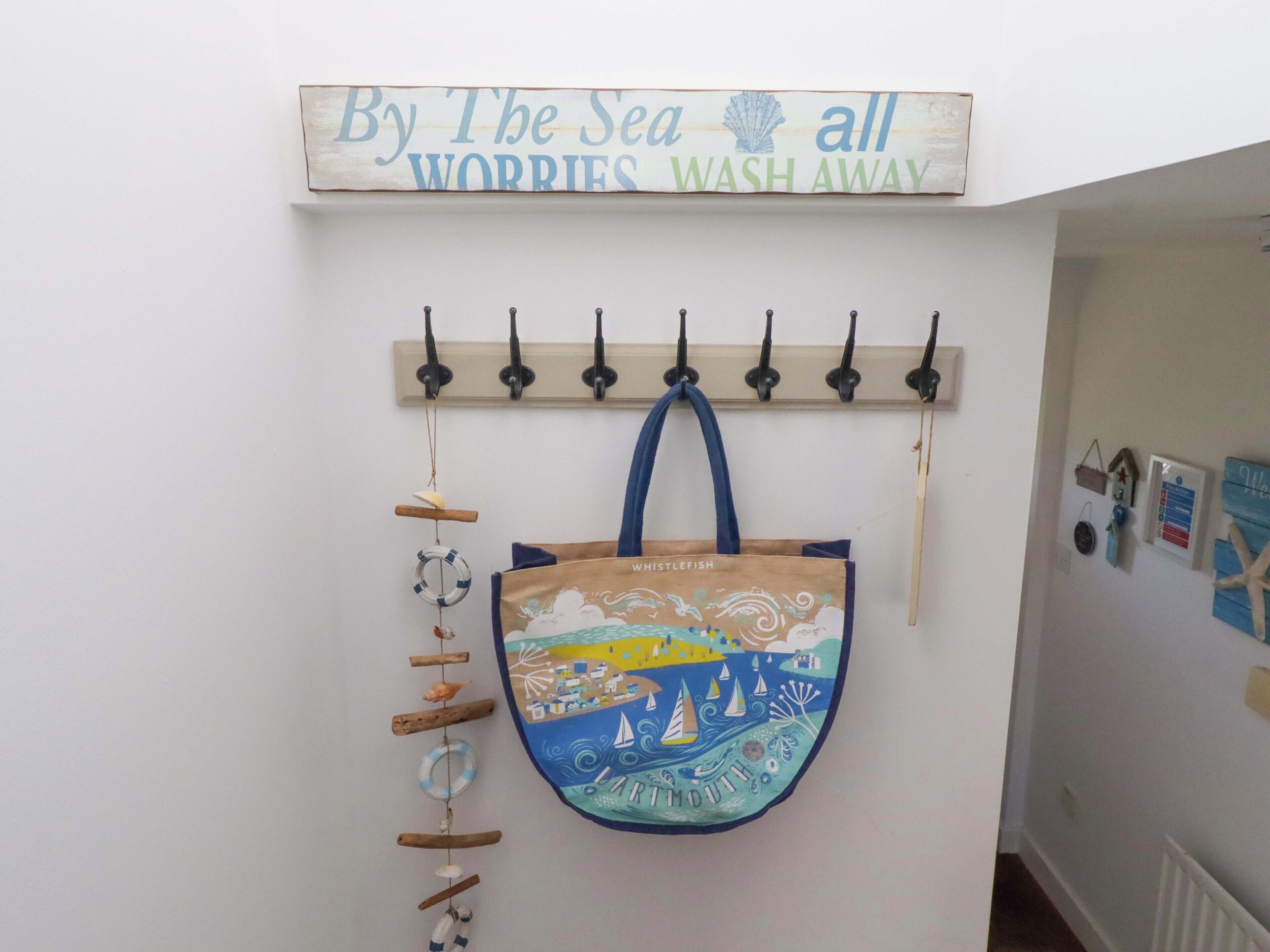A wall with a sign saying 'By The Sea all Worries Wash Away' and a hanging bag with a nautical design.