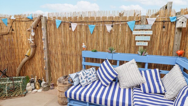 A blue and white striped outdoor seating area with a bamboo fence and decorative signs. - Tee View (Seahouses)
