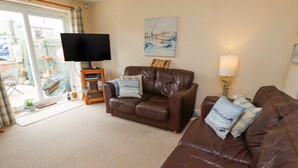 A living room with a brown leather sofa, a television, a painting of boats, and a lamp. - Tee View (Seahouses)