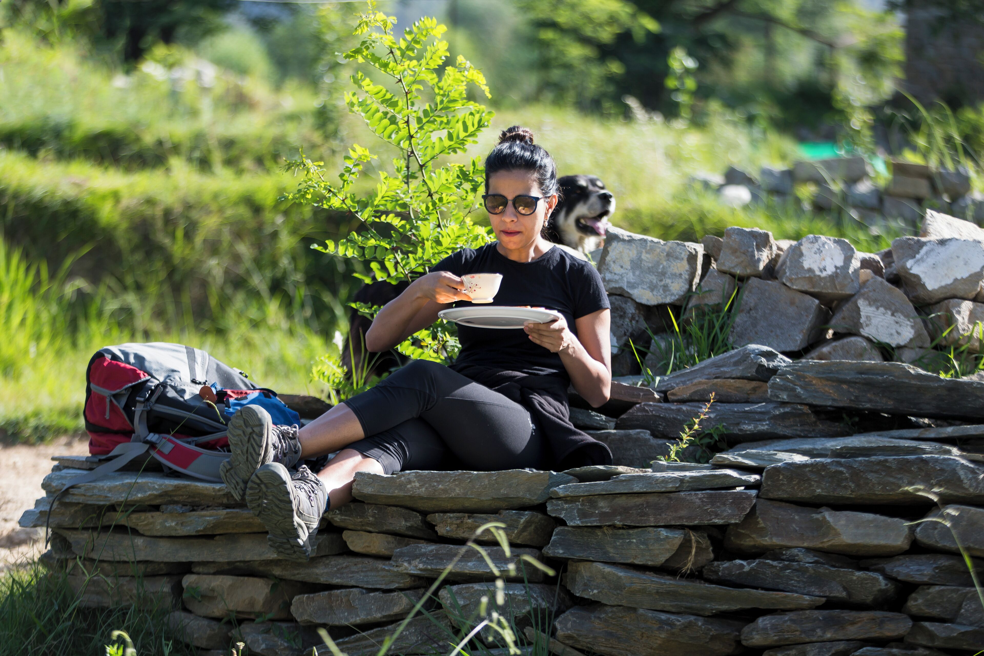 A person sitting on a stone wall with a backpack and a plate.