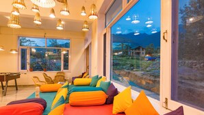 A room with a large window, colorful cushions, a foosball table, and hanging lights. - Dormigo  (Baijnath)