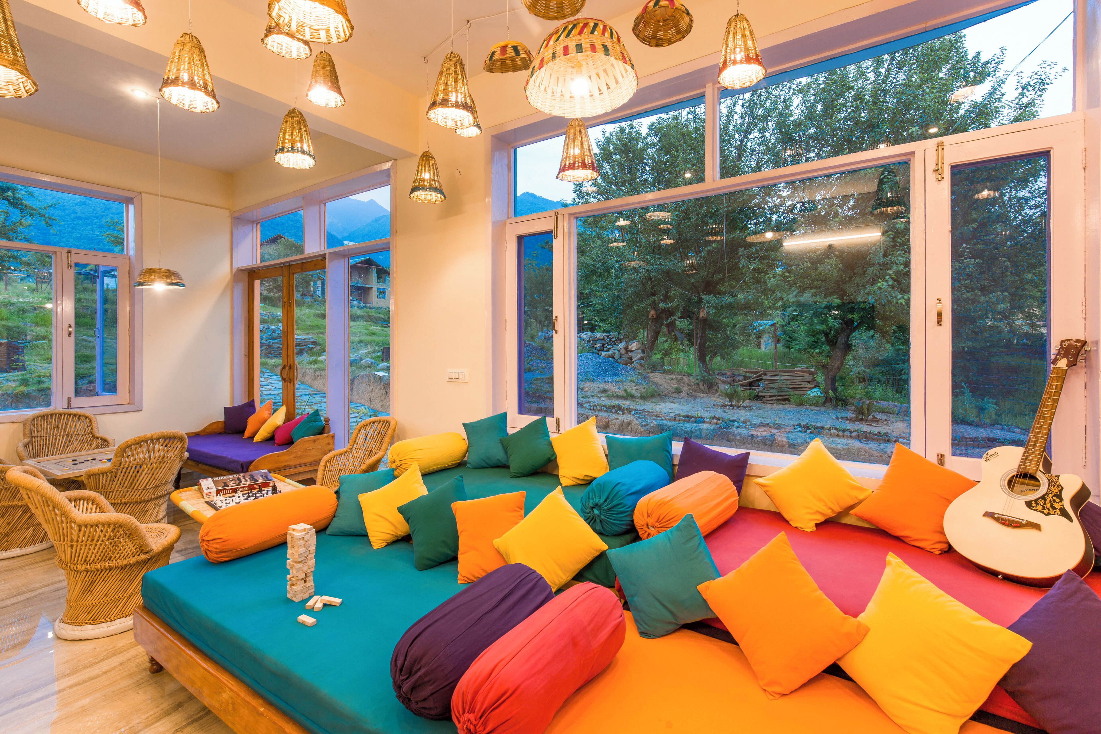 Une pièce spacieuse avec un grand lit, des coussins colorés, des meubles en osier et une guitare.