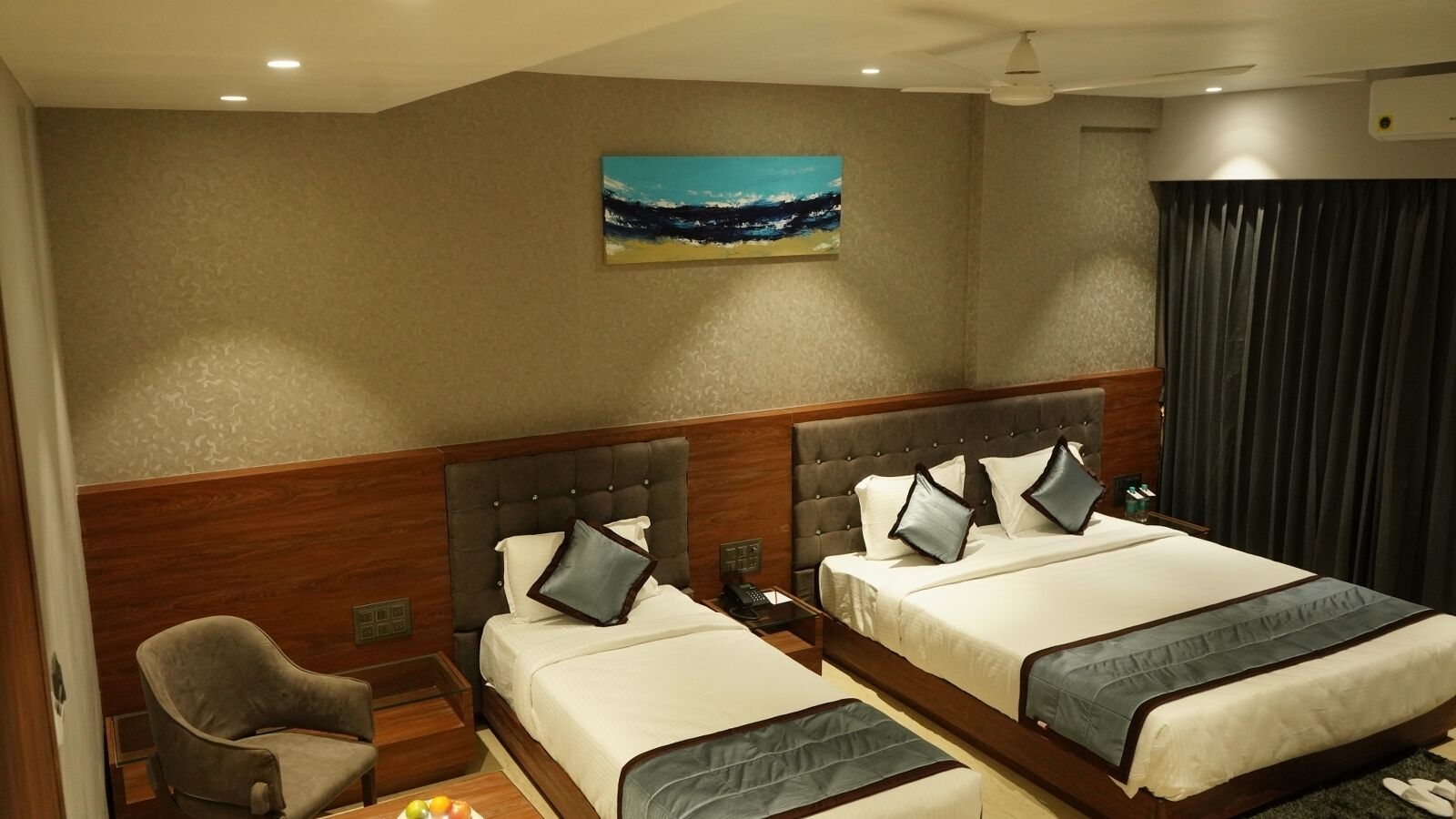 A hotel room with two beds, a chair, a painting of a beach, and a window with curtains.
