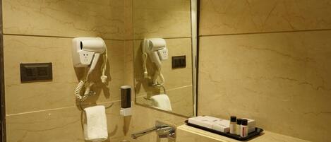 Un baño con pared de mármol, un perchero, un espejo, un secador de pelo, un lavamanos y una bandeja con artículos de aseo.