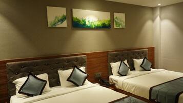 Habitación de hotel con dos camas, cada una con cabecero capitonado, ropa de cama blanca y almohadas decorativas. Hay tres obras de arte colgadas en la pared sobre las camas.