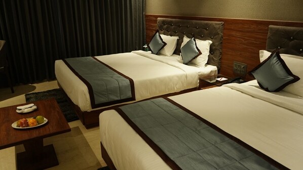 Quarto de hotel com duas camas, uma mesinha com frutas e uma mesinha de cabeceira com telefone.