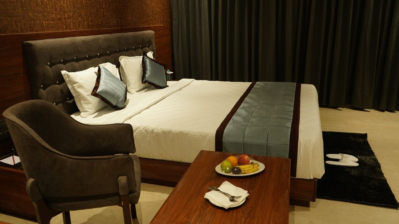 Une chambre d’hôtel avec un lit, une chaise, une table avec des fruits et une serviette, et un tapis noir.