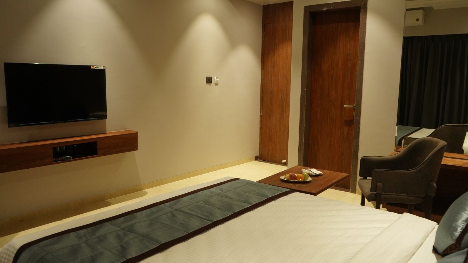 A hotel room with a bed, a TV mounted on the wall, a small table with a plate of food, and a chair.
