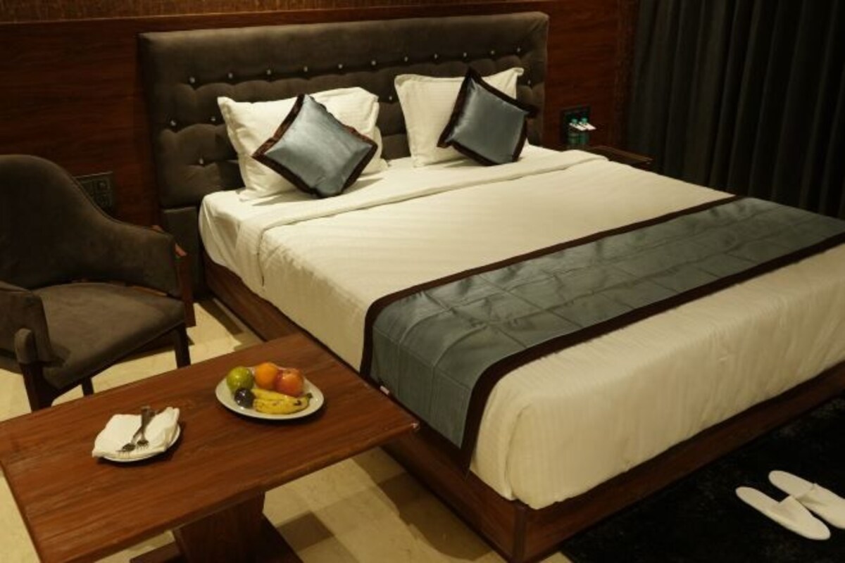 A hotel room with a large bed, a wooden nightstand with a plate of fruit, a chair, and a small table.