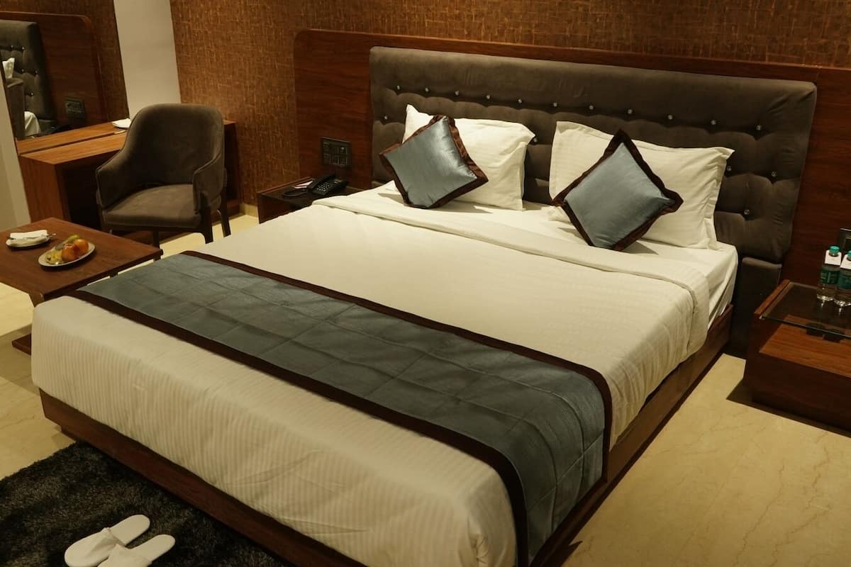Une chambre d’hôtel avec un grand lit, une table de chevet en bois, une chaise et une petite table sur laquelle se trouve une assiette de fruits.