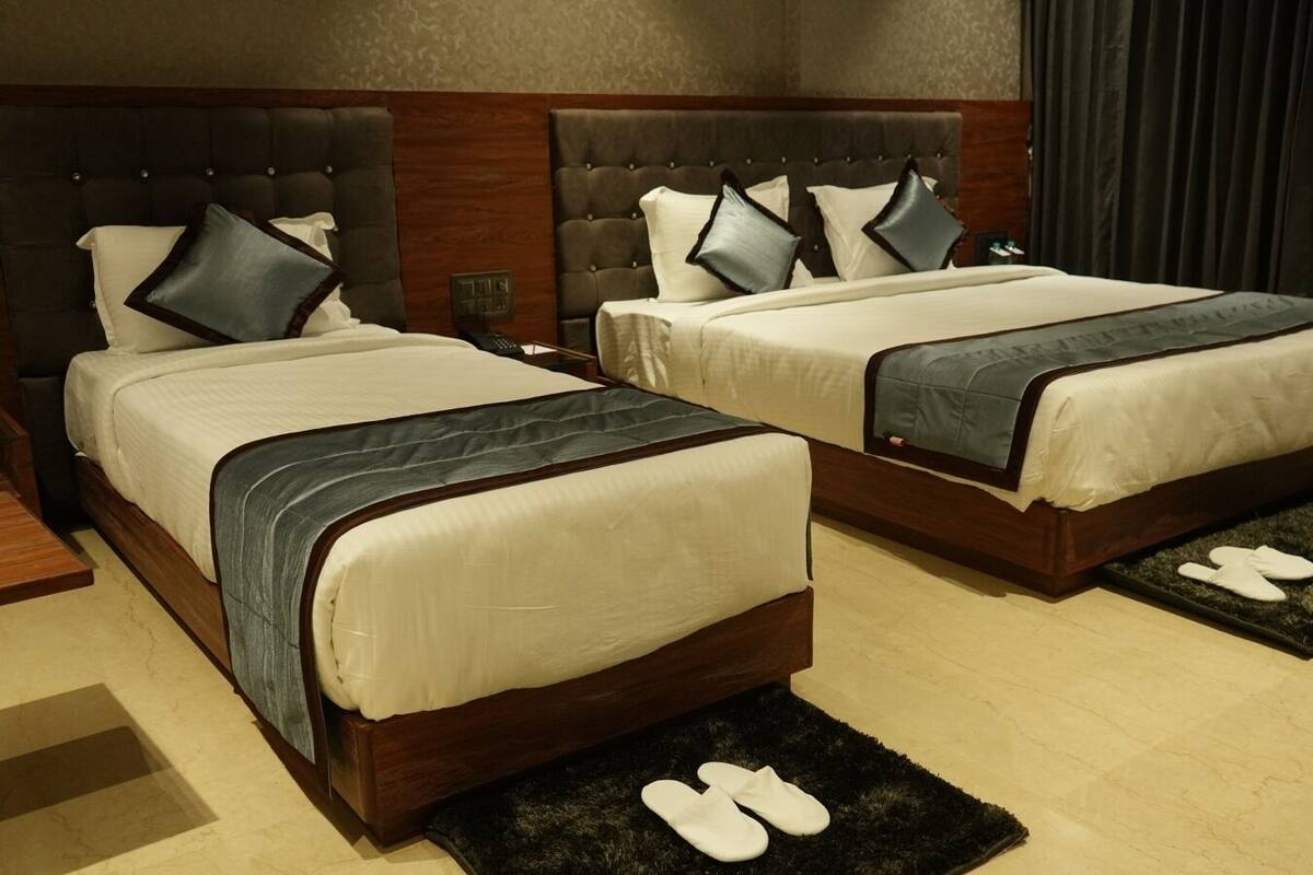 Une chambre d’hôtel avec deux lits, chacun doté d’une tête de lit en bois et de draps blancs. On trouve des chaussons sur un tapis noir devant chaque lit.