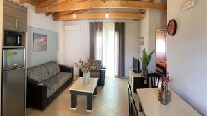 A cozy living room with a wooden ceiling, a sofa, a coffee table, a TV, and a dining area with a table and chairs.