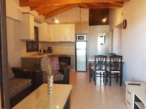 Een ruimtelijke woonruimte met een kitchenette, een eethoek en een zithoek met een bank en salontafel.