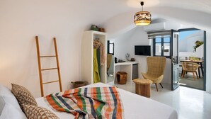 A bedroom with a bed, a ladder, a desk, a chair, and a balcony with a table and chairs. - Amphora Helios Gem - Private Jacuzzi and Views (Santorini)