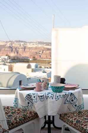 A table with a white tablecloth and blue patterns, set on a balcony with a view of buildings and mountains.