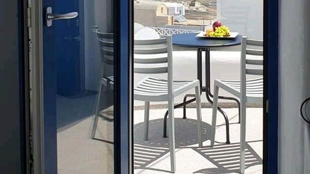 Ein Balkon mit Tisch und Stühlen, eine blaue Tür und Blick auf die Landschaft.
