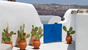 Eine Dachterrasse mit weißen Wänden, Terrakottatöpfen mit Kakteen, einer blauen Tür und freiem Blick auf eine gebirgige Landschaft.