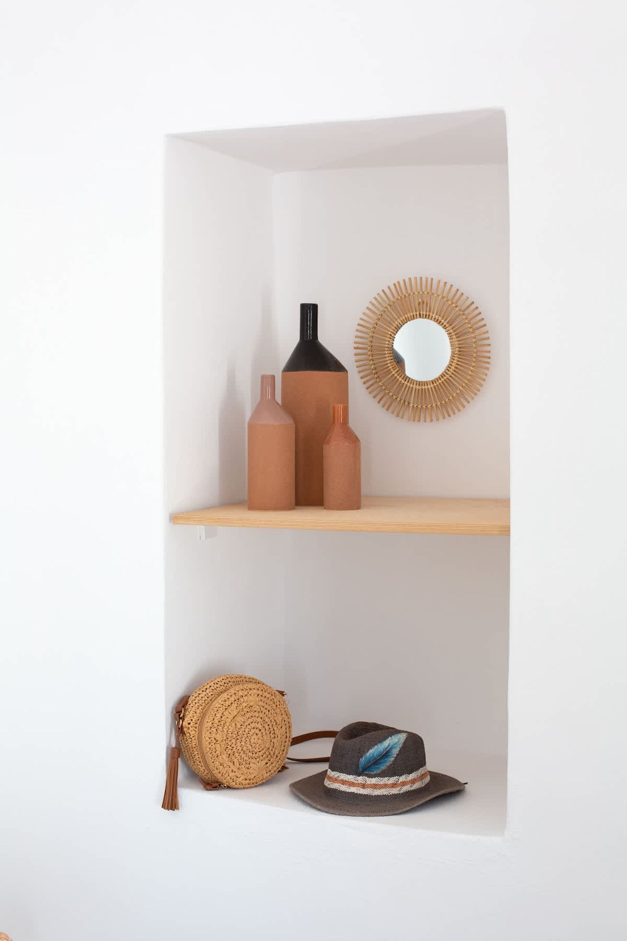 A shelf with three ceramic bottles and a woven bag.
