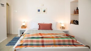 Ein Schlafzimmer mit einem Bett, zwei Nachttischen mit Lampen, einer farbenfrohen Decke, einem kleinen Teppich und einem Wandregal mit Dekoration.
