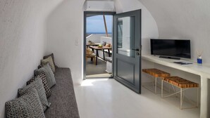 A modern living room with a grey sofa, a flat-screen TV, and wooden stools. - Amphora Selene Seaview Getaway in Akrotiri (Santorini)