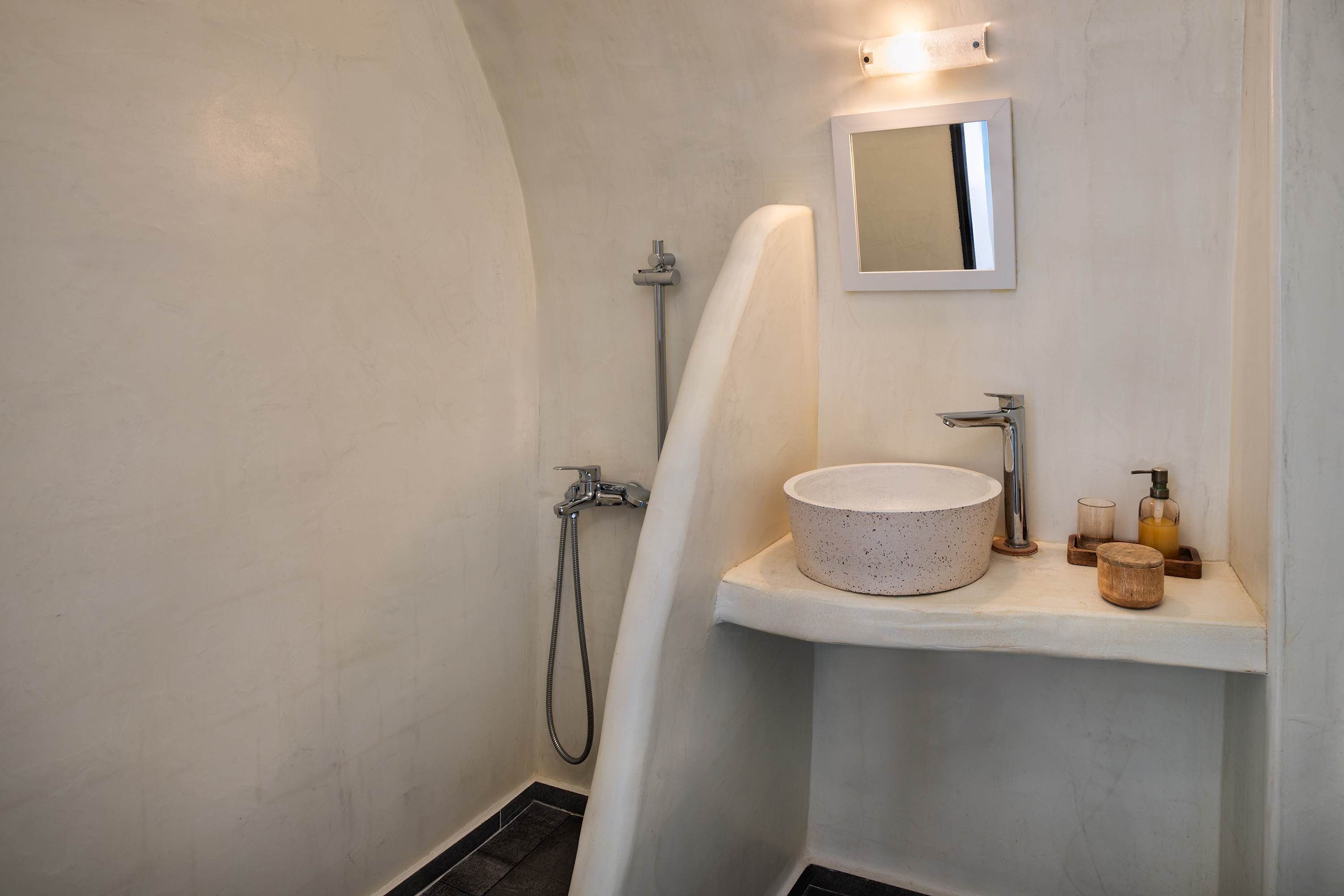 Un baño moderno con una bañera independiente, un lavabo redondo y un espejo pequeño.