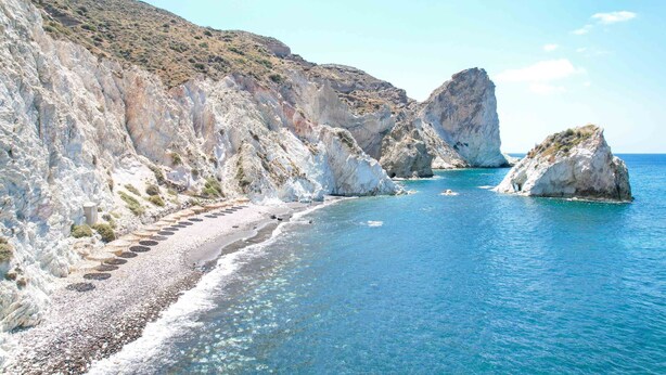 A coastal landscape with a pebble beach, rocky cliffs, and clear blue waters. - Amphora Selene Seaview Getaway in Akrotiri (Santorini)