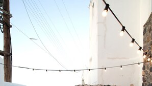 Una terraza en la azotea con una mesa y sillas, cactus en macetas, luces colgantes y vistas del paisaje.