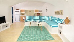 Un espacio habitable compacto con sofá, una mesita de centro, zona de cocina y televisor.