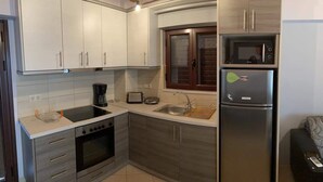 A compact kitchen with a stove, oven, microwave, and refrigerator. There is a window above the sink and a wooden ceiling beam.