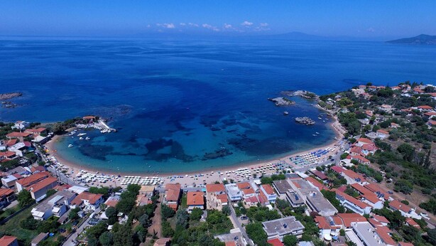 An aerial view of a coastal town with a beach, clear blue waters, and residential buildings.