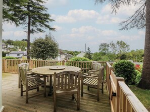 A wooden deck with a round table and chairs, surrounded by a wooden railing, overlooking a residential area with houses and greenery. - Fir Grove (Menai Bridge)