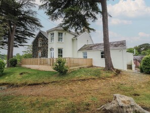 Una casa de dos pisos con fachada de piedra, terraza de madera y un patio cubierto de césped.