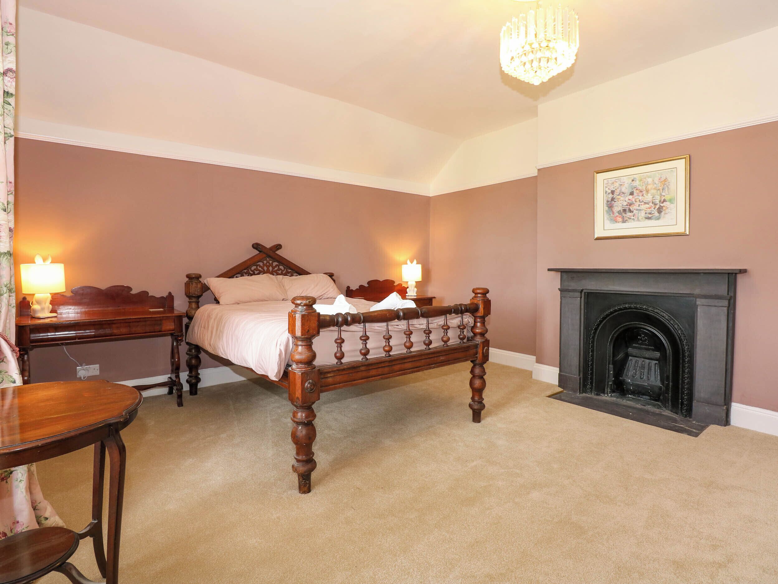 A bedroom with a four-poster bed, a fireplace, and a desk with a lamp.